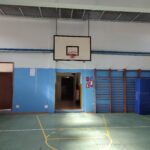 palestra della scuola secondaria di primo grado cavour con canestro da basket appeso sul soffitto, pareti bianche e azzurre, e pavimentazione verde con le strisce dei campi da basket e calcio