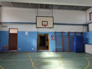 palestra della scuola secondaria di primo grado cavour con canestro da basket appeso sul soffitto, pareti bianche e azzurre, e pavimentazione verde con le strisce dei campi da basket e calcio