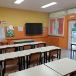 aula della scuola secondaria di primo grado di villafranca con lavagna interattiva, pareti gialle ed arancioni e banchi con sedie di vari colori