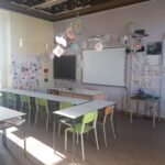 immagine di un'aula della scuola dell'primaria di garzigliana. Nell'aula ci sono banchi bianchi, sedie colorate, una lavagna interattiva ed una lavagna classica nera