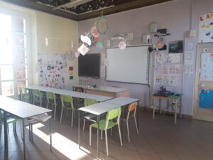 immagine di un'aula della scuola dell'primaria di garzigliana. Nell'aula ci sono banchi bianchi, sedie colorate, una lavagna interattiva ed una lavagna classica nera