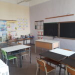 immagine di un'aula della scuola dell'primaria di garzigliana. Nell'aula ci sono banchi bianchi, sedie colorate, e due lavagne classice nere