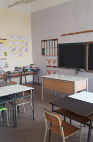 immagine di un'aula della scuola dell'primaria di garzigliana. Nell'aula ci sono banchi bianchi, sedie colorate, e due lavagne classice nere