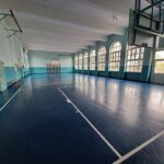 palestra della scuola primaria di villafranca. Le pareti sono di colore bianco e azzurro, il pavimento blu con le strisce del campo bianche. Sul soffitto sono appesi dei canestri.